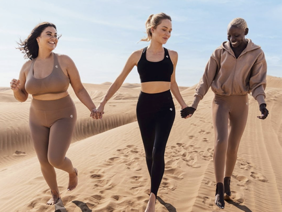 Tre ragazze in top e leggings che corrono sulla spiaggia
