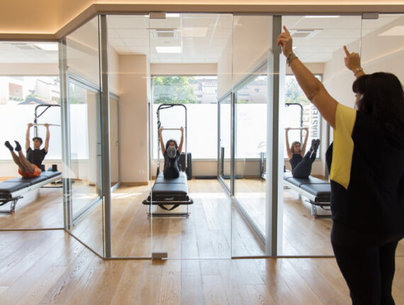 insegnante Pilates guida 3 clienti sul reformer in stanze separate da vetri